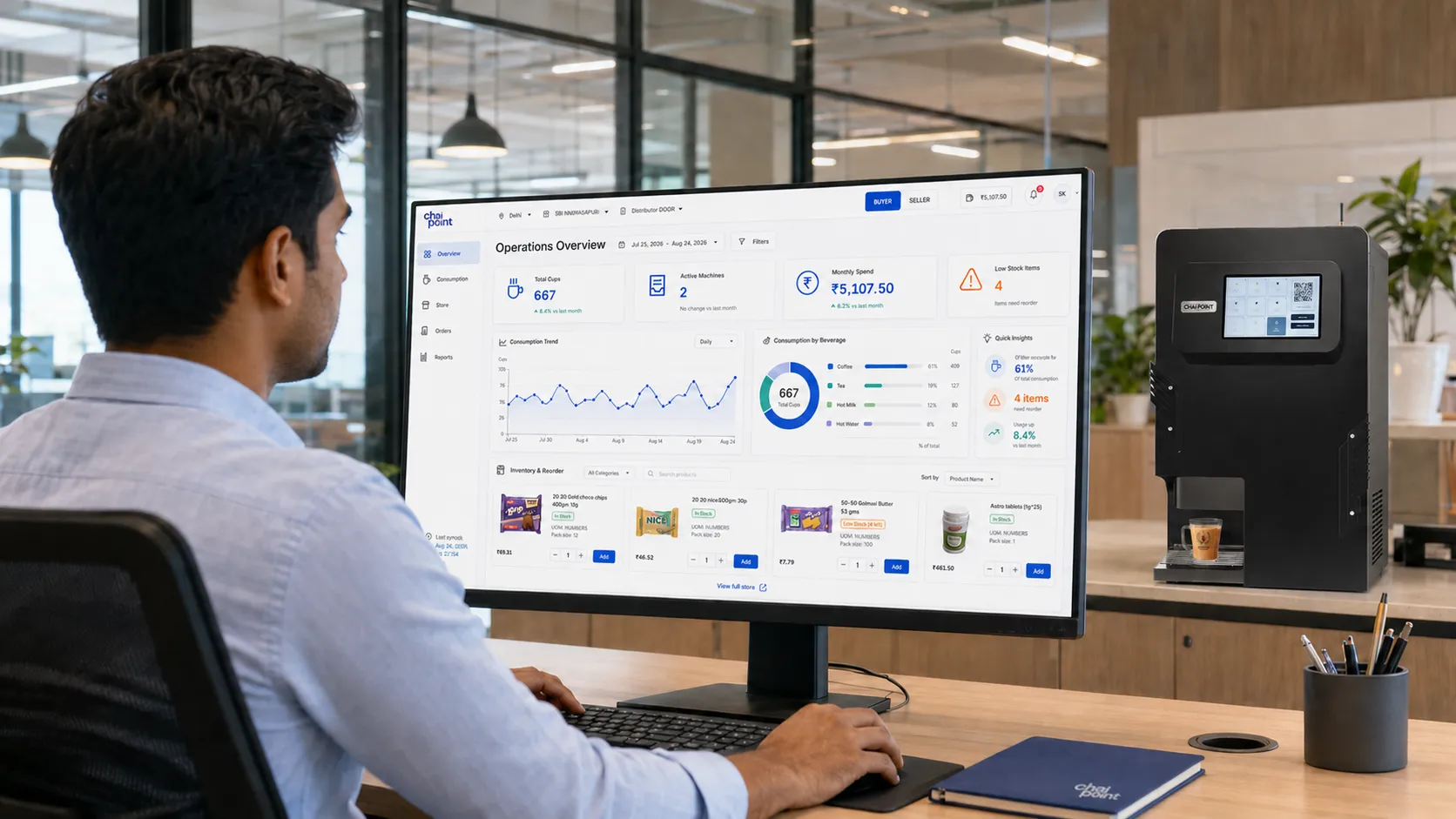 An office worker reviewing the BrewKart operations dashboard on a desktop monitor, a Brewing Bot beside the desk